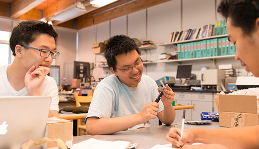 Three male students cooperate during their physics lab.